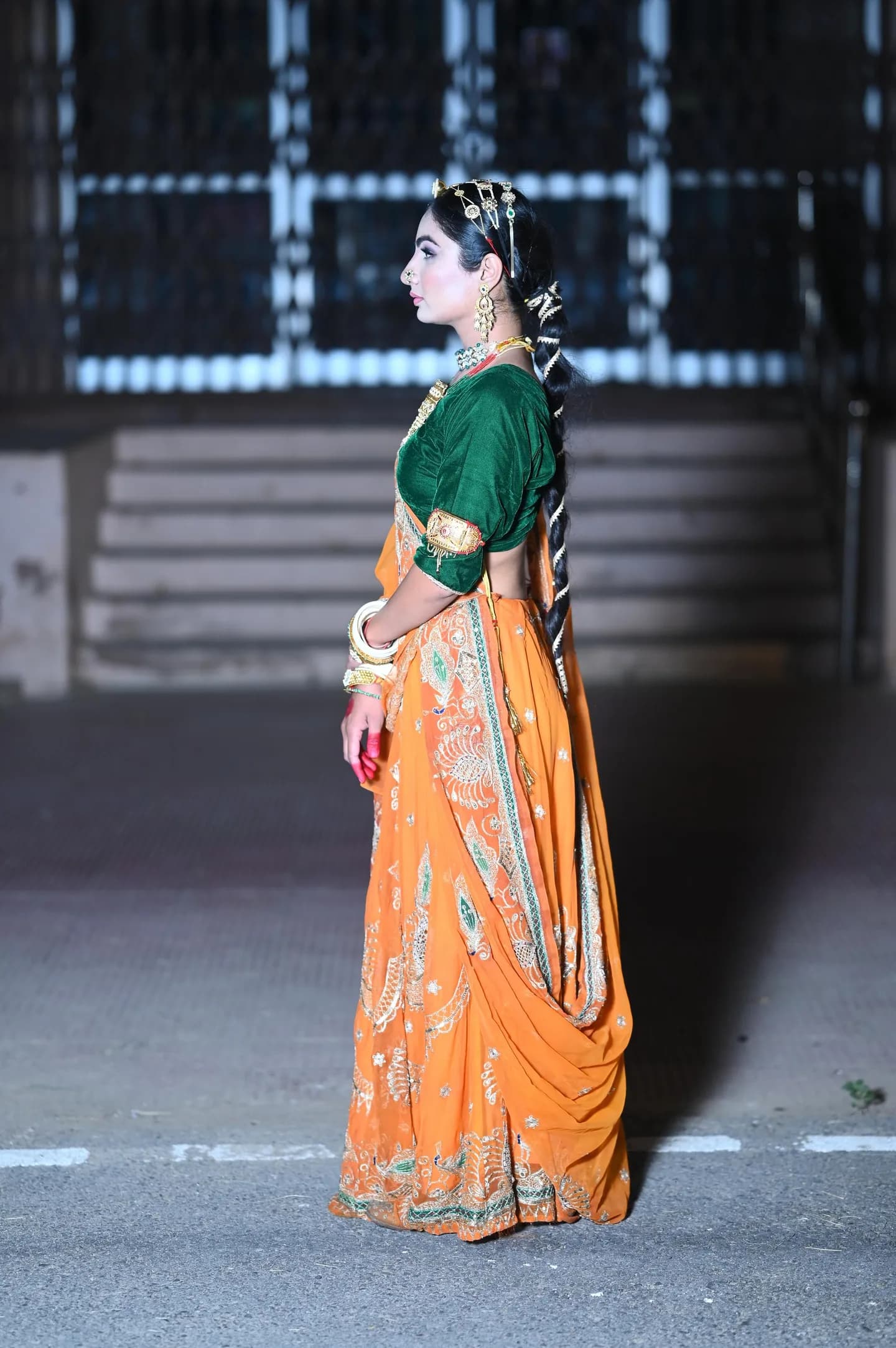 Full-length look in an orange saree with a long dressed braid, at night